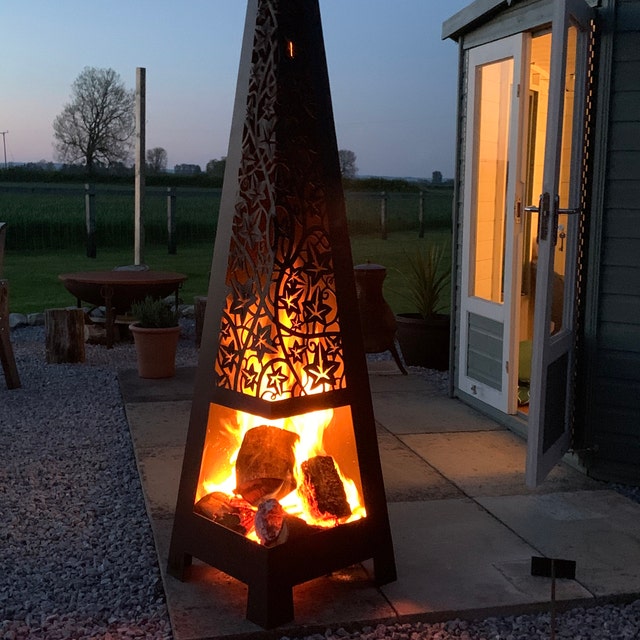 Matte black garden chiminea with ivy cut out design on a patio